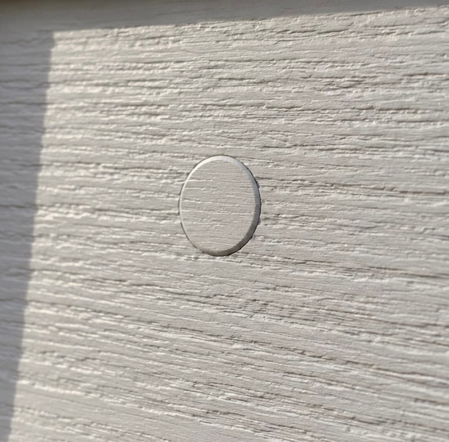 Illustration of a small round pre-wire plug set flush in textured lap siding