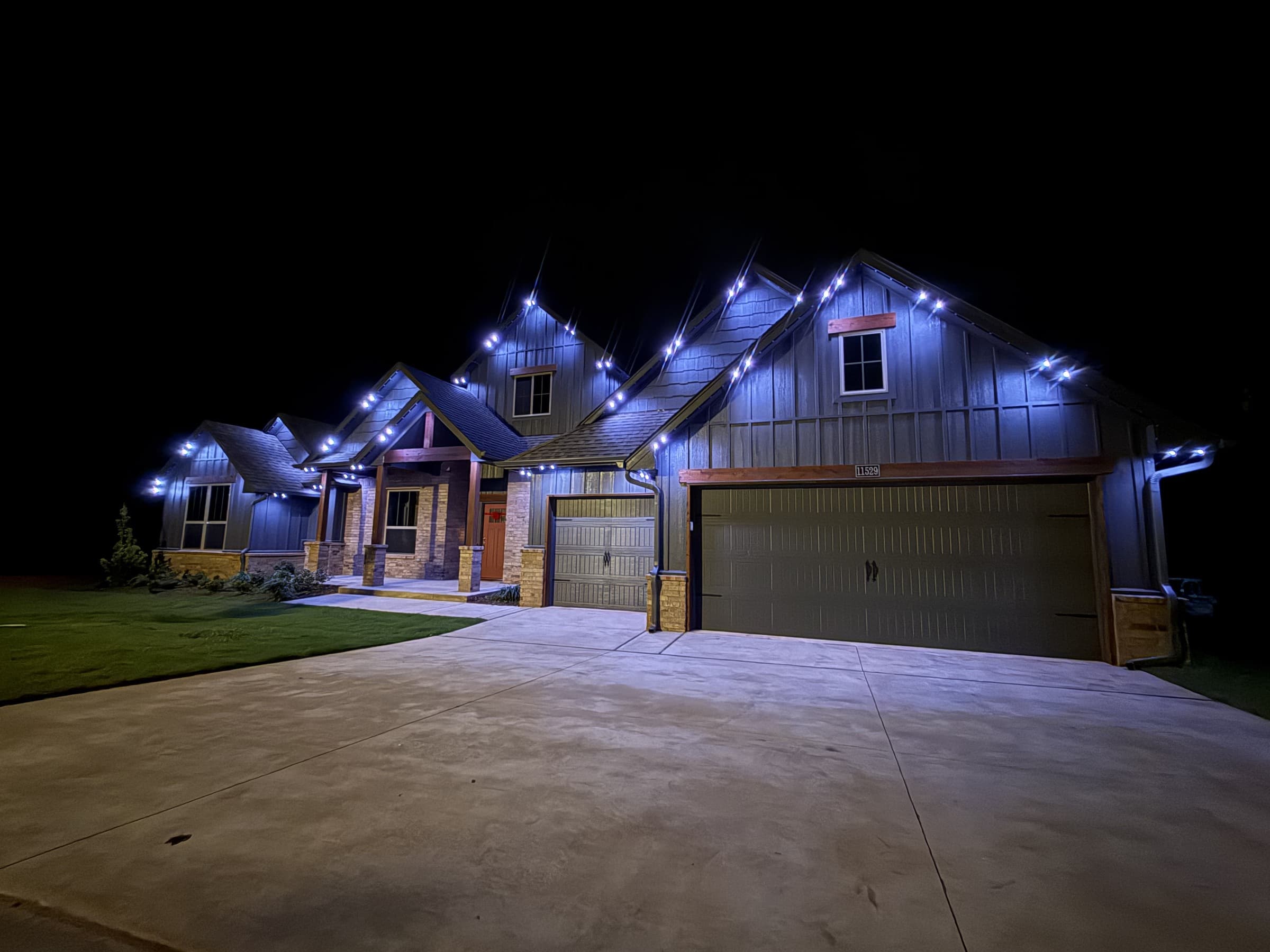 Multi-gable mixed-material home with TruLight permanent lighting set to a bright cool-white roofline effect.