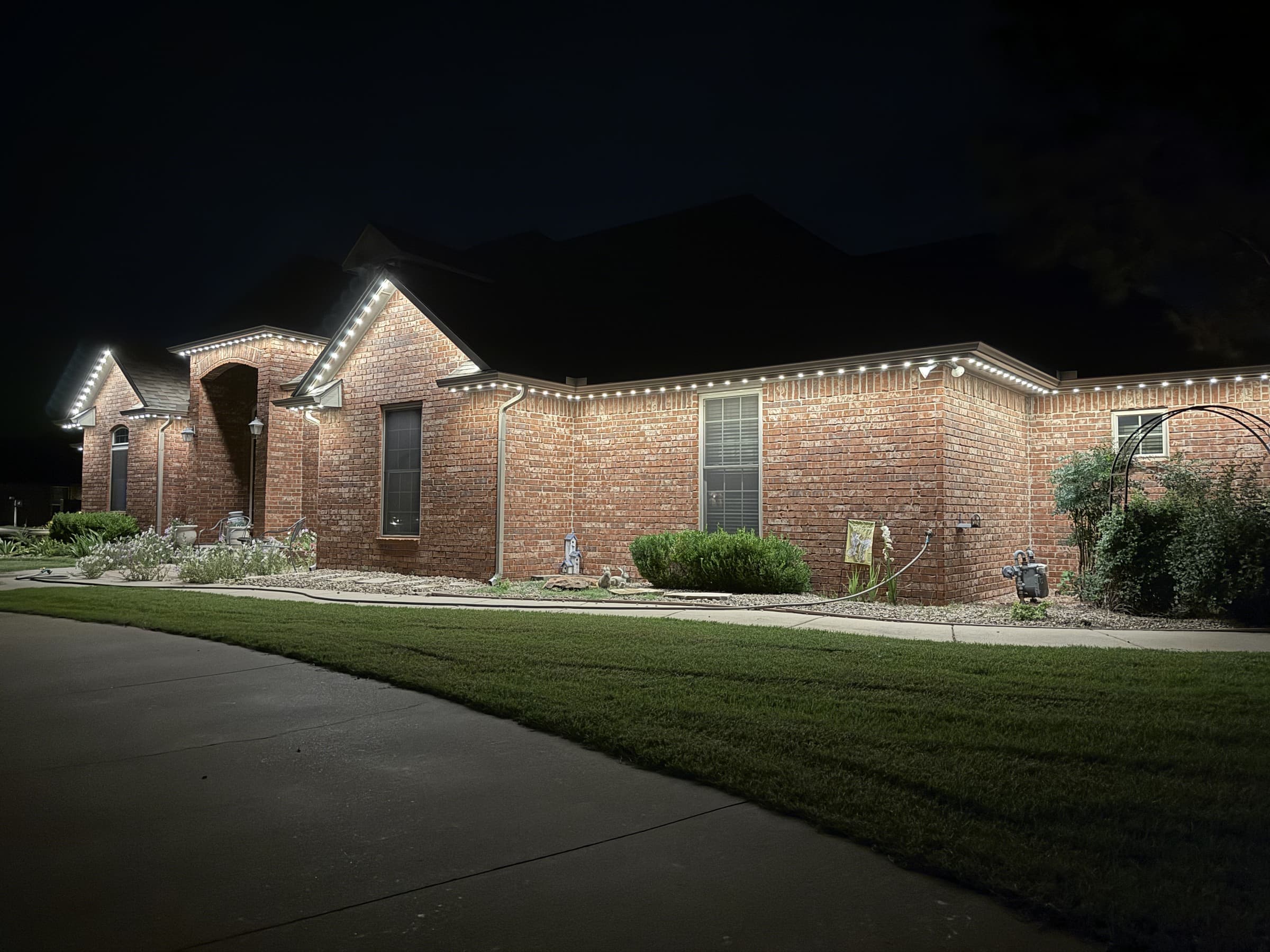 Single-story brick home with long eaves and TruLight permanent lighting set to a neutral-white roofline effect.