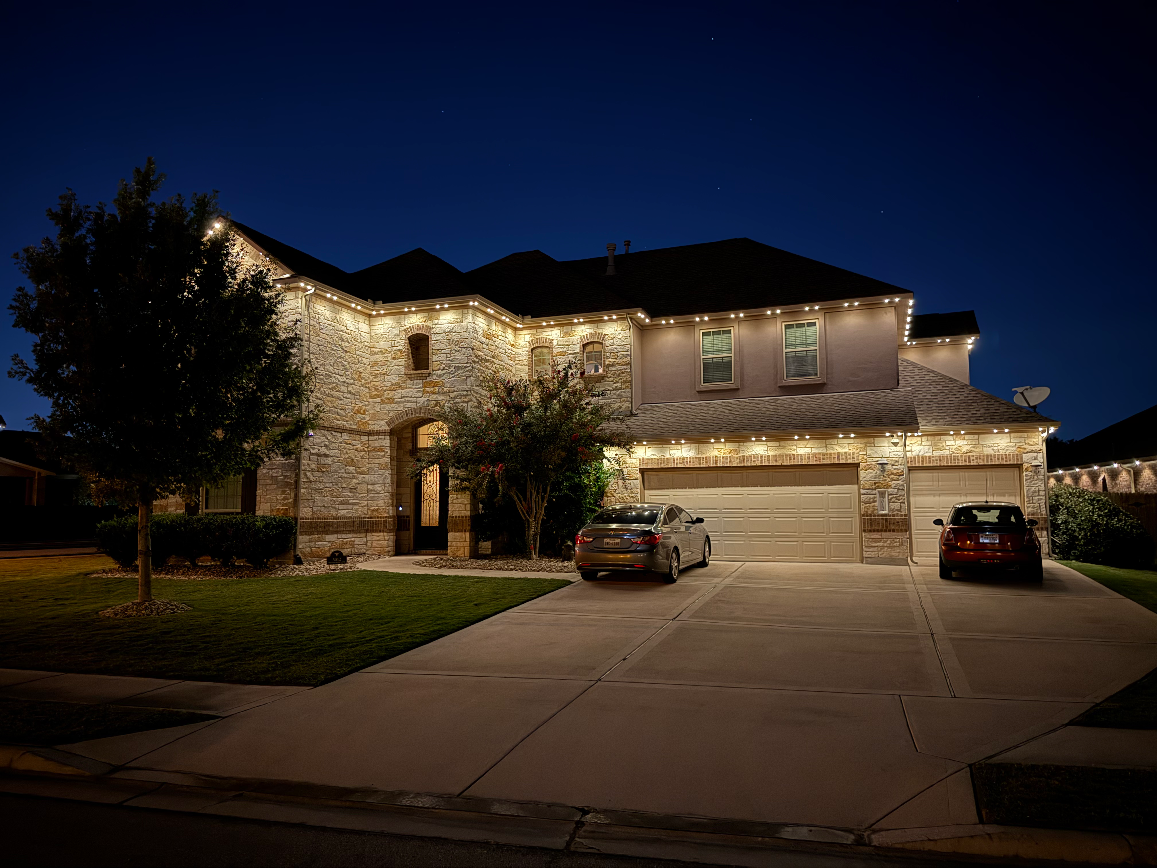 TruLight manufacturer example: Two story stone home with full roofline and garage white LED lighting